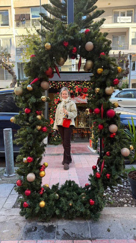 Фотозона в виде овальной хвойной рамки, внутри которой человек делает селфи на цветной пешеходной улице Измира с праздничными игрушками.