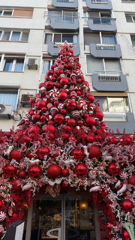 Фасад кафе полностью украшен красными шарами и гирляндами, образуя высокую насыщенную рождественскую композицию на улице Измира.