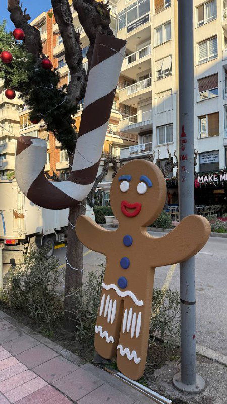 Декоративный пряничный человечек и большие украшения на дереве у тротуара — яркая тематическая фигура как часть рождественского оформления улицы.