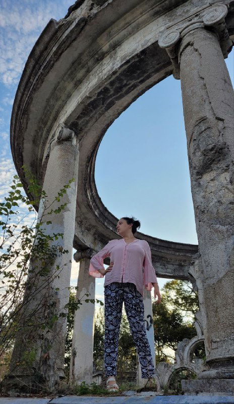 Женщина под круглыми колоннами развалин портика заброшенного ресторана на горе Ахун, виден небо и обломки вокруг.