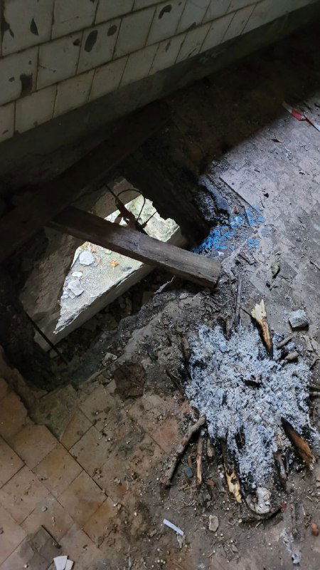 Внутренний вид разрушенного помещения: проломленный пол, остатки догоревшего костра, обломки плитки и мусор в катакомбах.