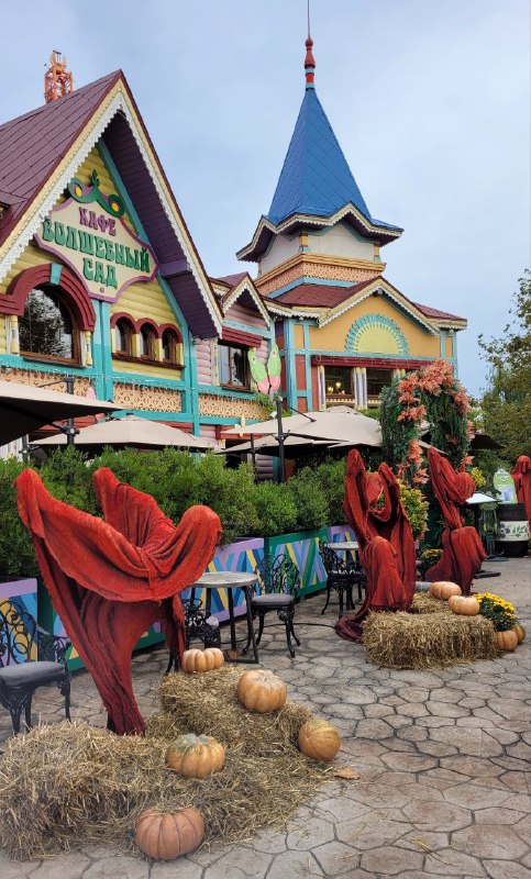 Красочные домики и торговые точки парка, украшенные тёмными тканями и осенними элементами, вокруг тыквы и снопы соломы для атмосферы.