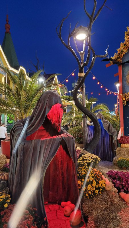 Красный свет освещает фигуры в капюшонах и осенние украшения вдоль аллеи парка, вечером создаётся кинематографичная атмосфера ужаса.