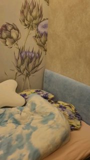 Ночная фотография спальни: низкая кровать с голубоватым пледом, декоративной подушкой и цветочным орнаментом на стене — уютная сцена.