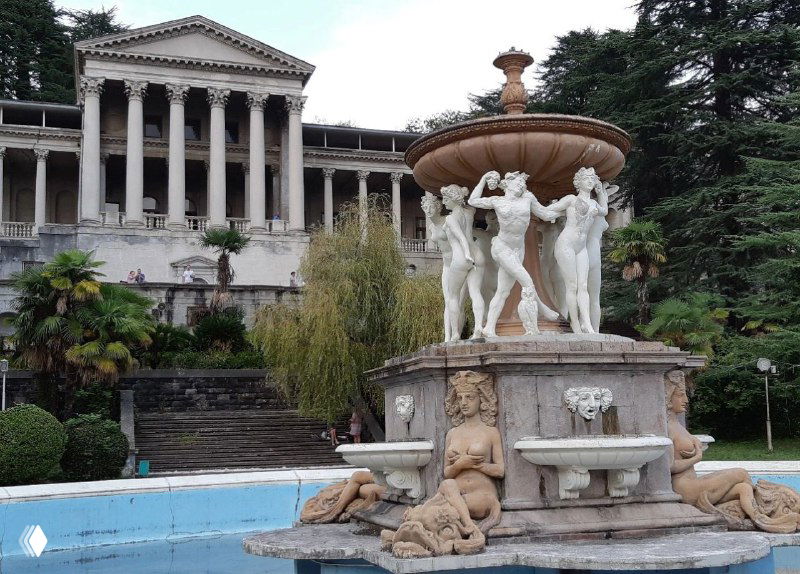 Широкий вид декоративного фонтана с несколькими скульптурами русалок и колоннадами корпуса санатория им. Орджоникидзе в Сочи