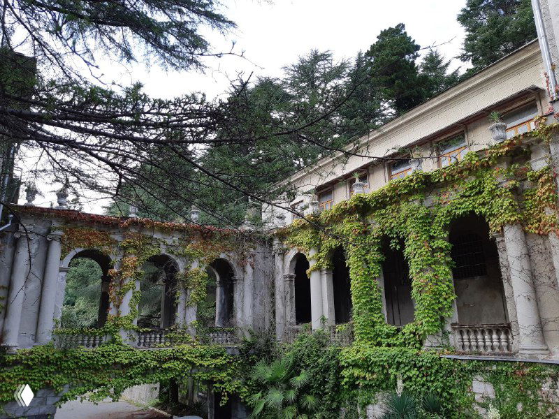 Внутренний двор с арочными колоннадами и густым плющом, заросшая каменная архитектура курортного комплекса в зелени.