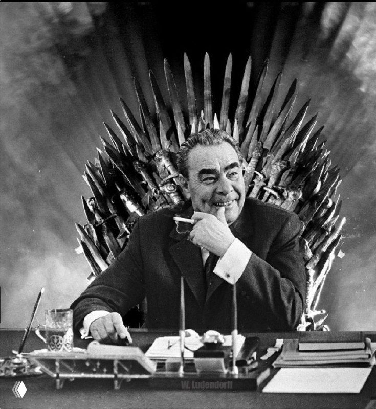 Чёрно-белая сатирическая фотография: мужчина в костюме за письменным столом, на фоне — массивный трон, театральный монтаж.