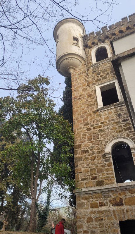 Каменная башенка старого замка или дворца среди деревьев: фасад с арками и пустыми окнами создаёт мрачную атмосферу и ассоциации с легендой.