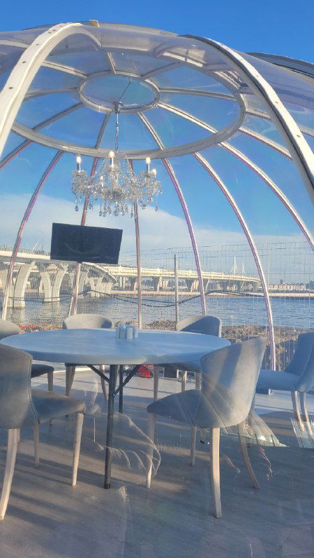 Интерьер купола с хрустальной люстрой, круглым столом и телевизором; панорамные окна открывают вид на морскую линию горизонта.