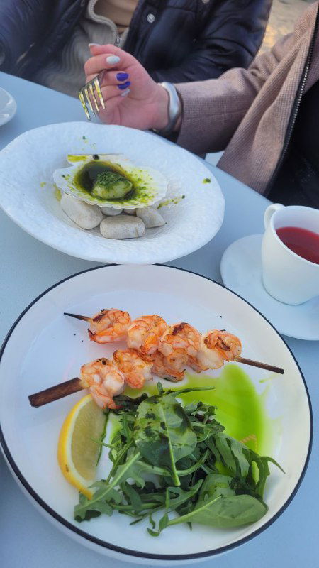 Тарелка с креветками на шпажках, зелёный гарнир и кружка с напитком — крупный план блюда, поданное в уличном шатре у моря.