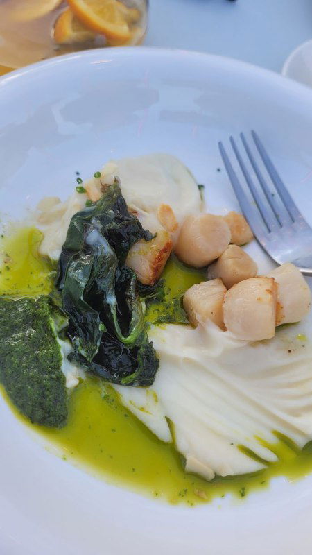 Крупный план гребешков в соусе с зелёными травами и текстурой блюда — аккуратная порция, снятая с близкого расстояния.