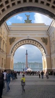 Вид через арку на Дворцовую площадь в Санкт‑Петербурге: Александровская колонна, прохожие и мягкий весенний городской свет.