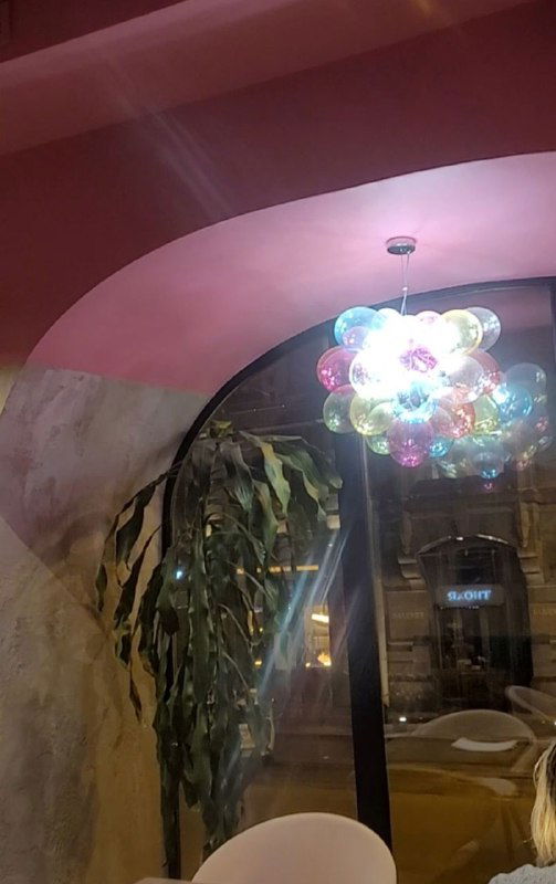 Люстра из связанных надувных шариков, подсветка создаёт праздничное настроение в интерьере шоколад-бара, растения у окна заметны рядом.