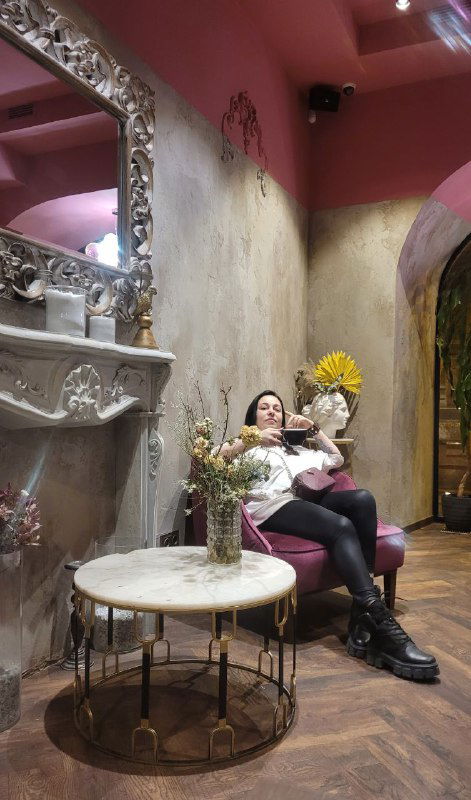Посетительница в кресле с букетом цветов в руках на фоне барочного зеркала и уютного уголка кафе, атмосферный интерьер Чоко.