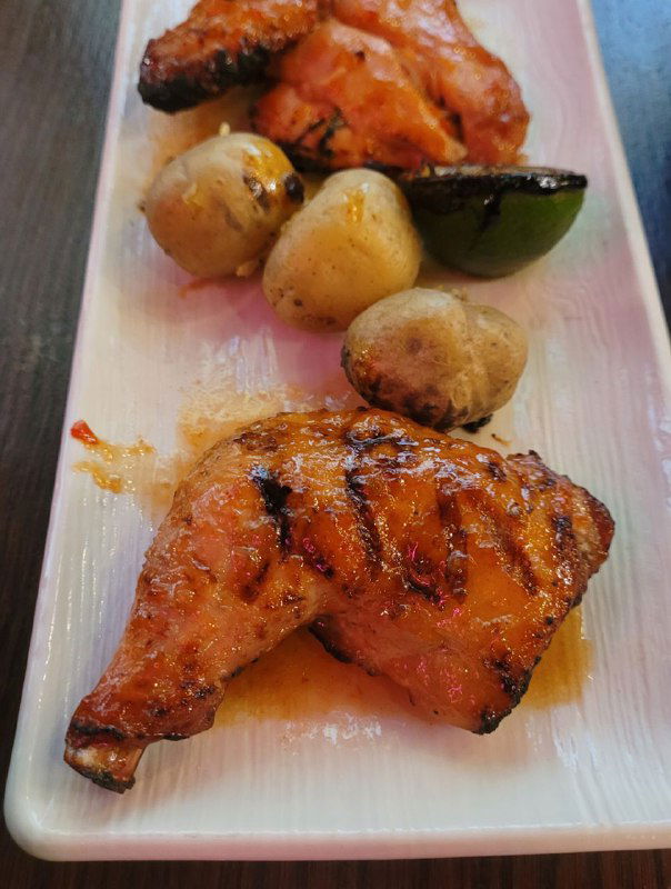 Крупный план: жареные куриные куски и шампиньоны на длинной тарелке, золотистая корочка и следы соуса после огненной подачи.