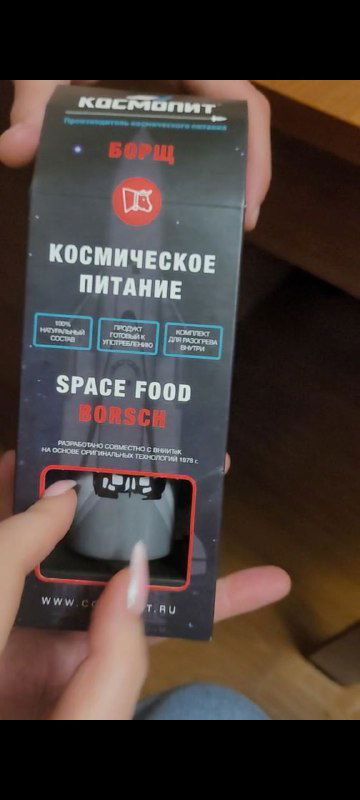 Общий ракурс коробки с вырезом, через который виден тюбик с надписью «БОРЩ», упаковка в руках — перспективный вид продукта.