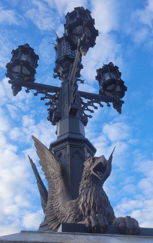 Крупный кадр фонарного столба с декоративной скульптурой птицы и небом, акцент на художественной ковке и бронзе