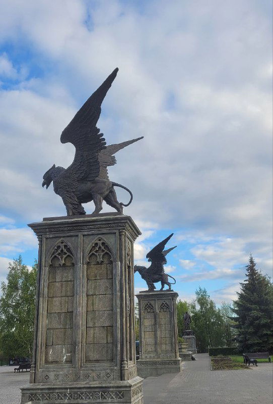 Фигуры крылатых существ на постаментах — декоративные скульптуры, подчеркнутые небом и архитектурной облицовкой