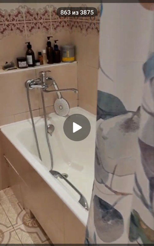 Ванная комната с ванной, шторкой и полками для косметики; стандартная светлая отделка и бытовые предметы.