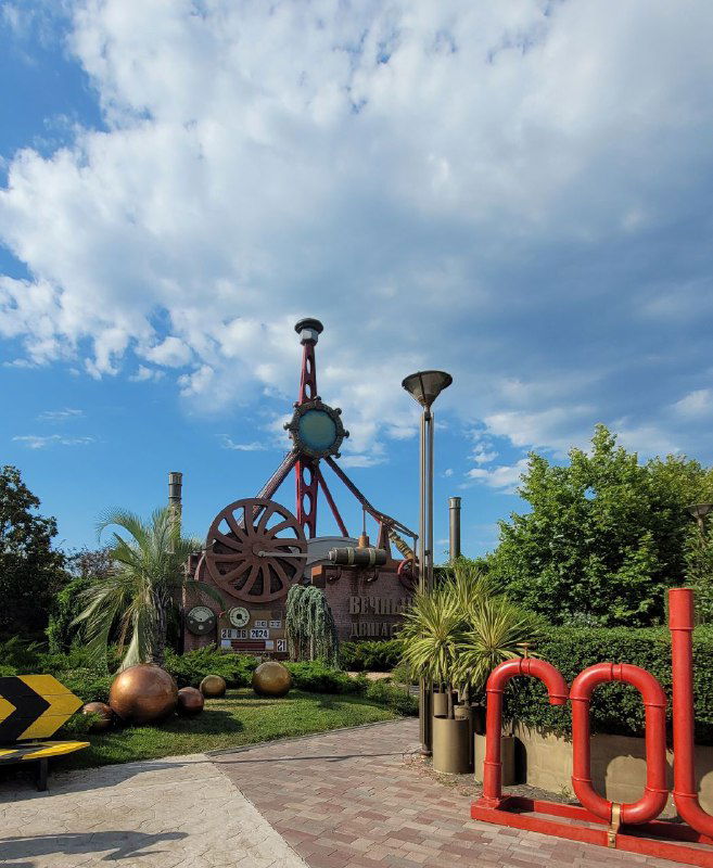 Общий план стимпанк‑локации у ресторана: шестерёнки, лампы и архитектурные элементы на фоне голубого неба, видна дорожка вокруг здания.