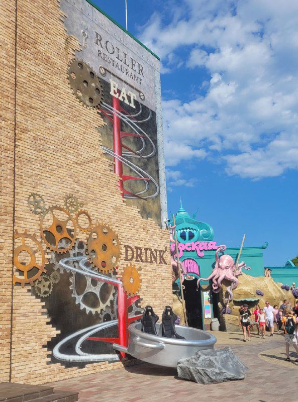 Стена заведения с графикой и спиральной рельсой для подачи напитков/еды; видны буквы "DRINK" и декоративные детали в стиле стимпанк.