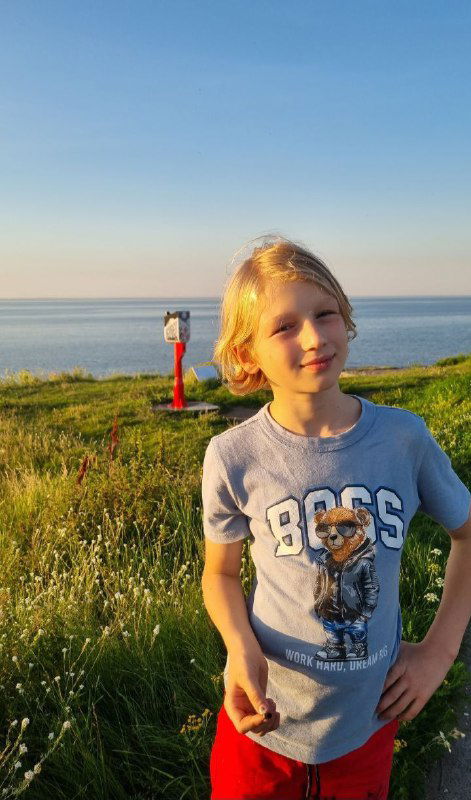 Портрет ребёнка на фоне моря и травы в тёплом вечернем свете: расслабленная поза, мягкие тени и летняя атмосфера Кронштадта.