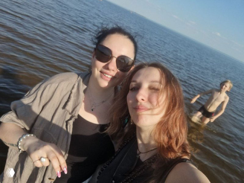 Селфи двух женщин на фоне моря: близкая композиция, улыбки, отражение закатного света и тихая прибрежная сцена в Кронштадте.
