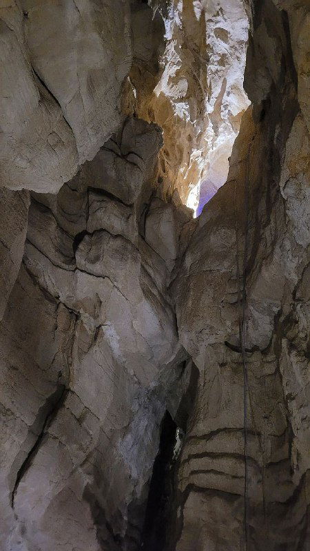 Высокие вертикальные сталактиты и узкие просветы в верхней части пещеры, видна глубина карстовой системы под землёй.