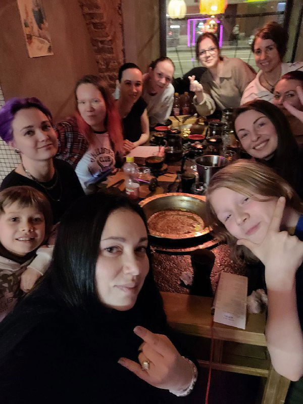 Ещё одна групповая селфи-фотография в кафе: улыбающиеся люди вокруг горячих блюд, атмосфера дружеской встречи и обсуждения практических схем.