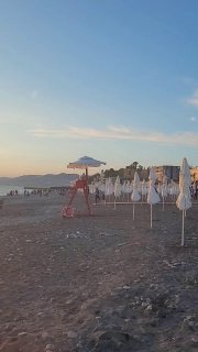 Пляж с рядами зонтиков и спасательной вышкой на фоне моря; пустой песок и прибрежная линия в тихий курортный вечер у Черного моря.