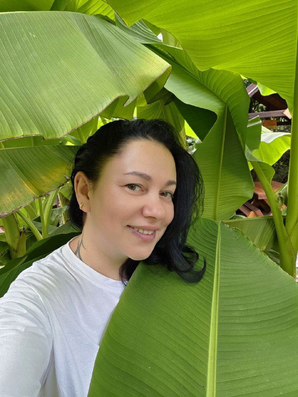 Селфи автора на фоне больших банановых листьев: лицо в кадре, крупные зелёные листья создают тропическую атмосферу.