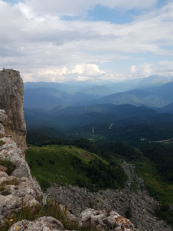 Широкая горная панорама с обрывом и дальними хребтами в Адыгее: вид с утёса показывает сложный рельеф и пространства для пеших маршрутов и игр на природе.
