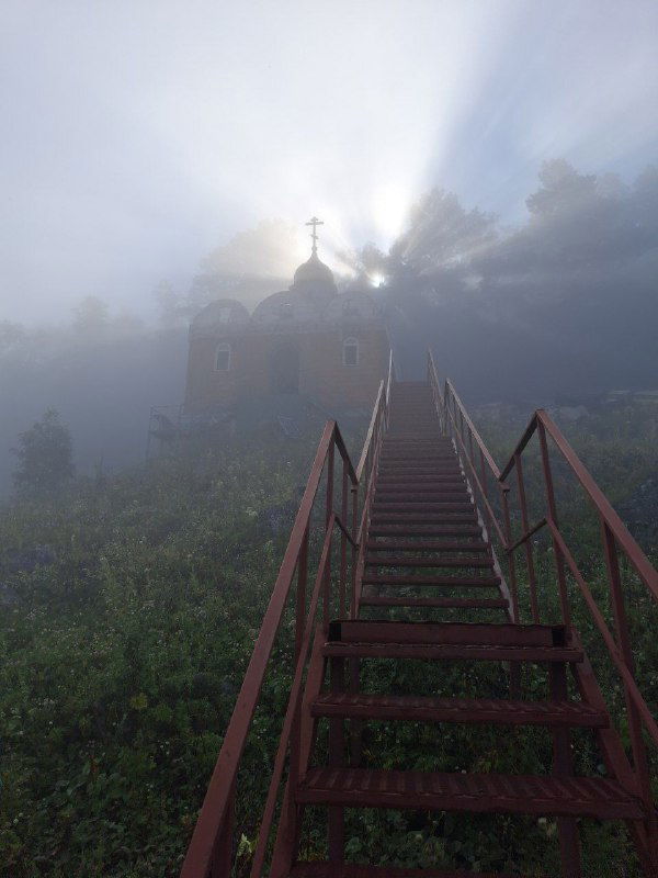 Утренняя туманная сцена с небольшой горной церковью: лестница, ведущая к кресту, мягкий рассветный свет и мистическая атмосфера в горах Адыгеи.