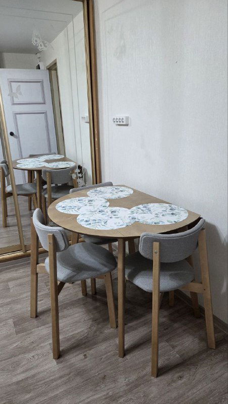 Компактный обеденный стол с четырьмя стульями у зеркальной двери, светлые тона и простая сервировка — деревенская, но аккуратная обеденная зона.