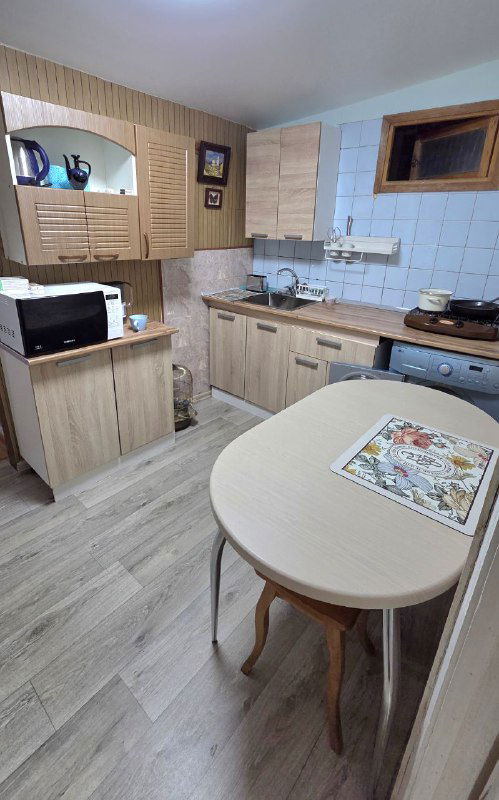 Кухонная зона с деревянными фасадами, рабочей поверхностью, микроволновкой и небольшим столом — простая функциональная кухня в деревенском стиле.