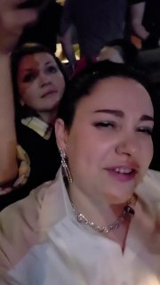 Кадр: женщина в толпе поёт и эмоционально реагирует на выступление, на фоне видны мигрирующие сценические огни и люди.