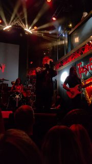 Широкий план сцены и публика: прожекторы, дым и артисты в центре внимания, видна сцена клуба и зрители у барьера.