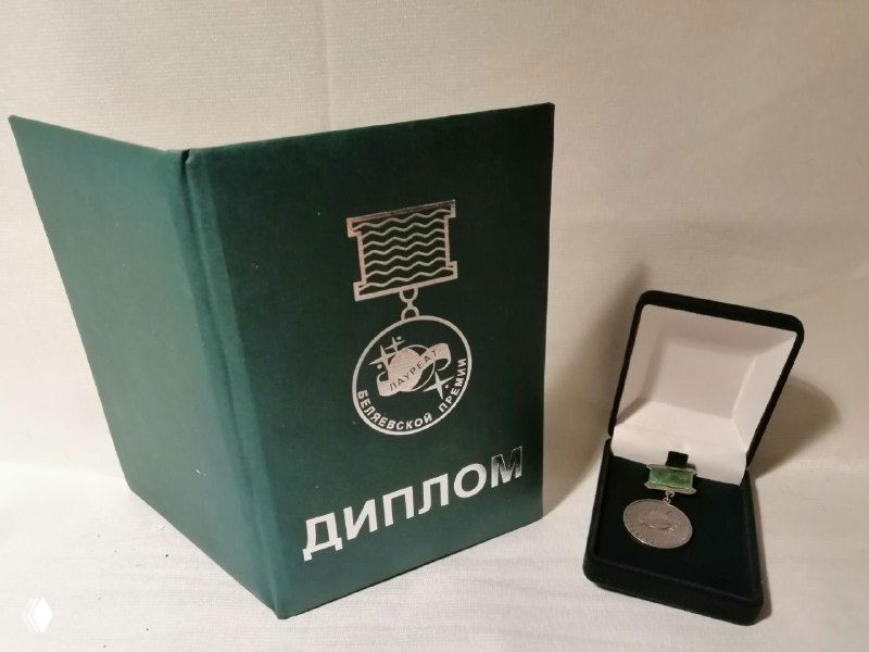 Зелёный переплёт диплома с тиснением «ДИПЛОМ» и медаль в футляре на столе; композиция подчёркивает наградной характер публикации и торжественный момент.