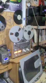 Фото гаража с аудиоаппаратурой: крупные магнитофонные бобины, радиола 1950‑х и усилители на полках — атмосфера тёплого аналогового звучания.