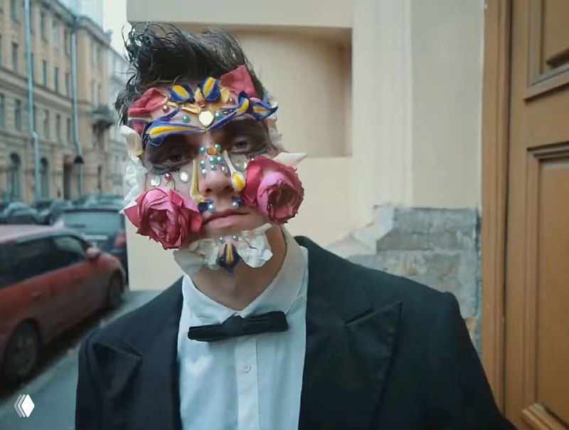 Ещё один кадр в уличной локации: мужчина в маске из роз и страз, лепестки на лице и эстетический декор в стиле зумер-тренда