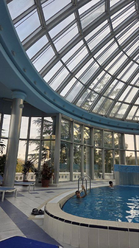 Ракурс на бассейн и фрагмент кругового борта, видно лестницу в воду, рядом полотенца и мелкие детали интерьера вокруг купола.