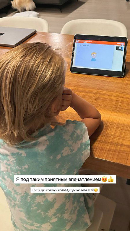 Ребёнок сидит за столом и смотрит на экран планшета с учебным содержимым; иллюстрация дистанционного занятия и вовлечённости ребёнка в учебу.