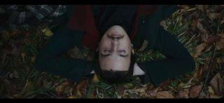 Кадр из фильма: молодой мужчина в старинном костюме лежит на опавших листьях в центре кадра, лицо обращено вверх, осенняя медитативная сцена природы.