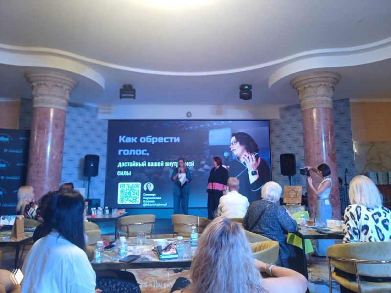 Спикер на сцене перед аудиторией, на экране виден слайд «Как обрести голос» — обучающее выступление в формате практикума.