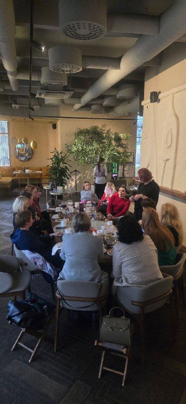 Ещё один ракурс той же встречи в кафе: круг людей за столом, амбиент кафе и обсуждение в непринуждённой обстановке.