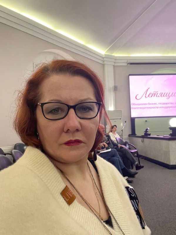 Портретное фото участницы конференции в светлом интерьере: близкий план, серьёзный деловой образ и фон зала мероприятия.