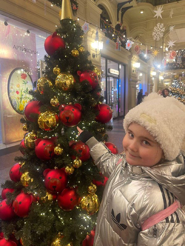 Ребёнок возле украшенной новогодней ёлки в торговом центре; праздничные гирлянды и рождественская атмосфера вокруг.