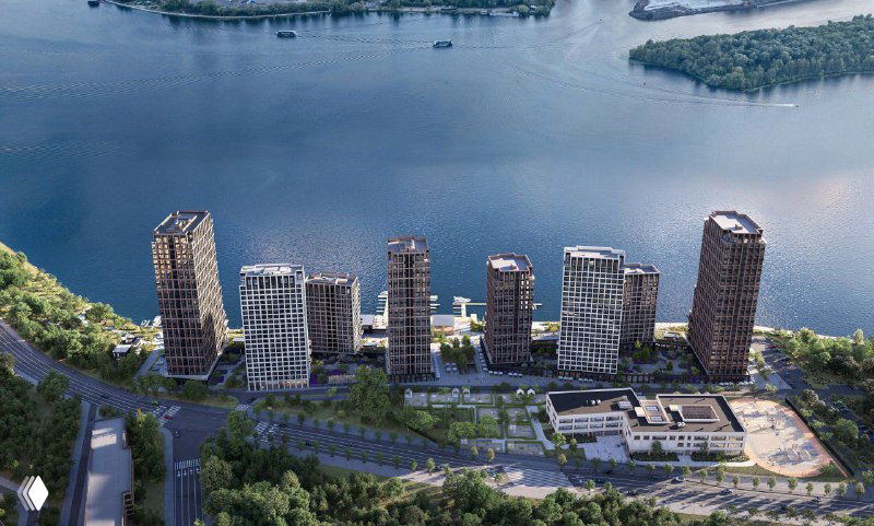 Вид с воздуха на жилой комплекс вдоль широкой глади Москвы‑реки: группа современных многосекционных домов, причал и набережная.