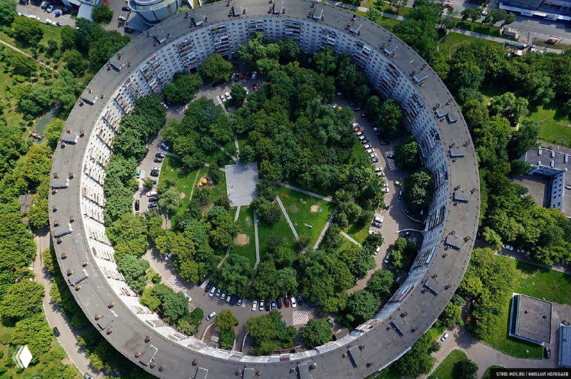 Вид сверху на дом-кольцо с внутренним двором, похожим на парк: озеленённая центральная территория и равномерная круговая застройка.