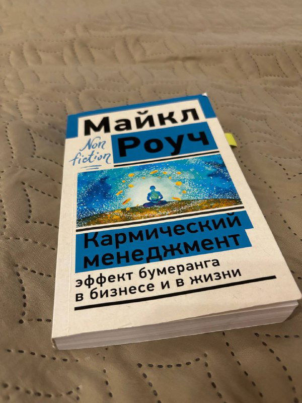 Книга «Кармический менеджмент» Майкла Роуч крупным планом на покрывале; видна обложка с подписью про эффект бумеранга в бизнесе и жизни.
